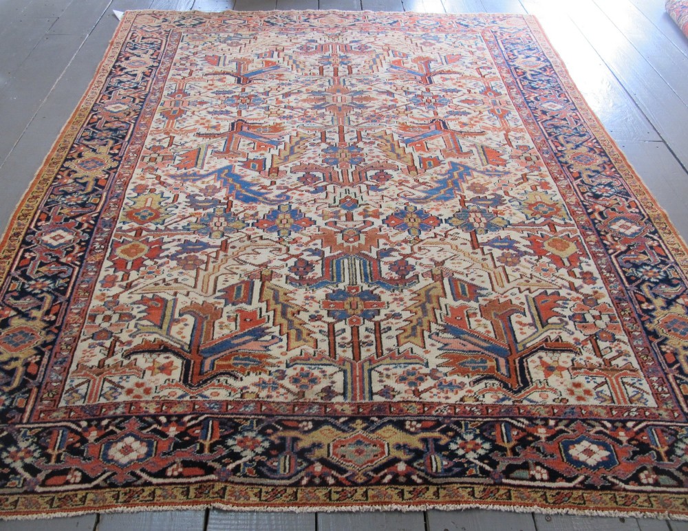 A large hand-knotted Persian Heriz rug featuring a central geometric medallion on an ivory background with terracotta and blue borders.