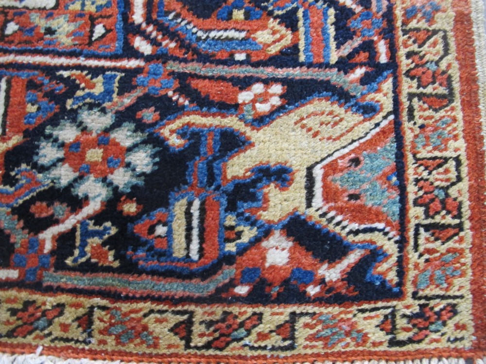 A large hand-knotted Persian Heriz rug featuring a central geometric medallion on an ivory background with terracotta and blue borders. View IV