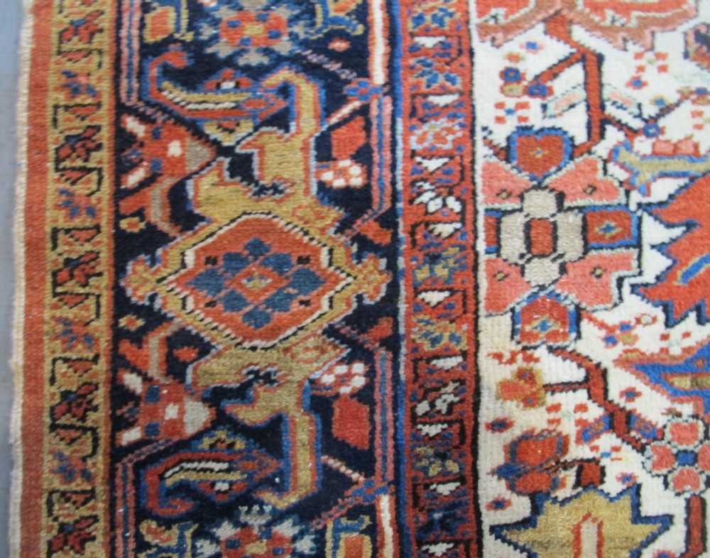 A large hand-knotted Persian Heriz rug featuring a central geometric medallion on an ivory background with terracotta and blue borders. View V