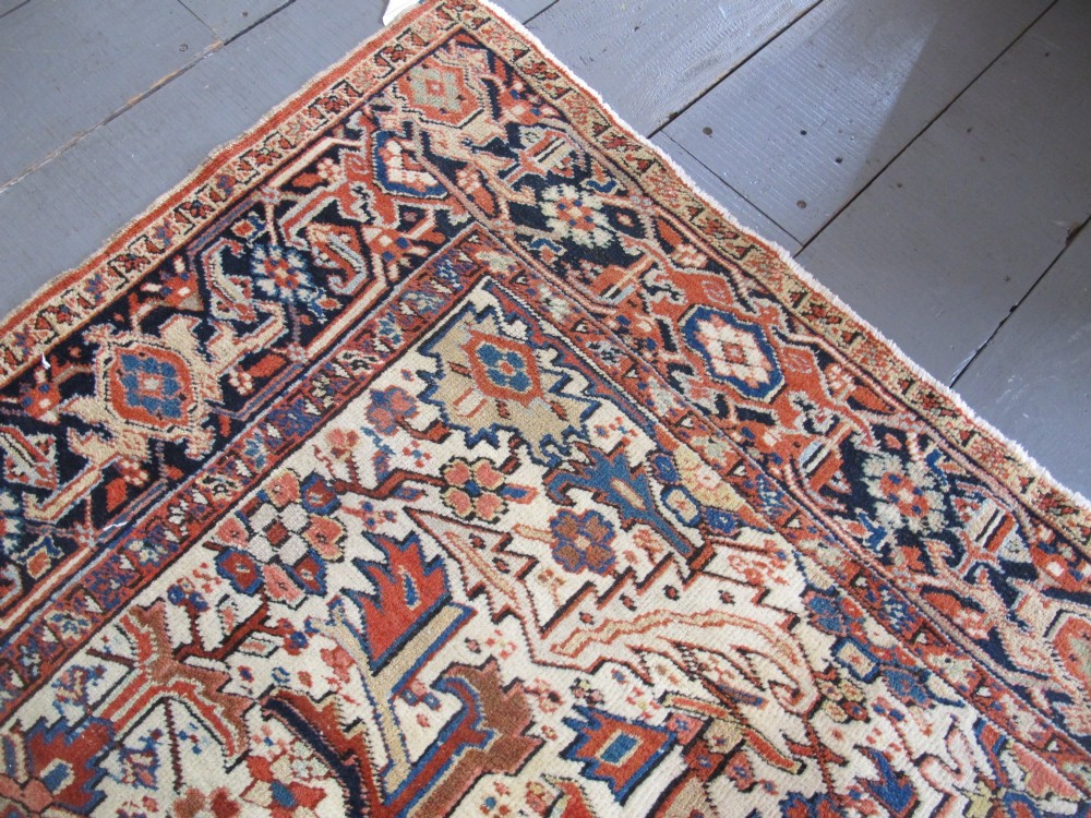A large hand-knotted Persian Heriz rug featuring a central geometric medallion on an ivory background with terracotta and blue borders. View VI