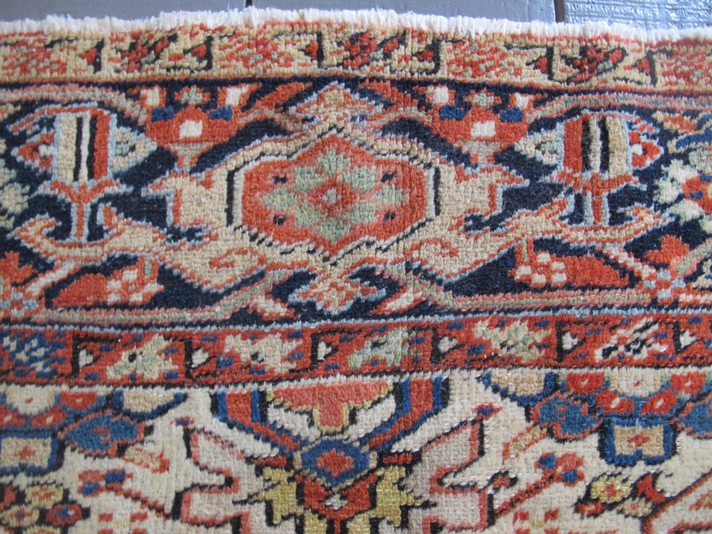 A large hand-knotted Persian Heriz rug featuring a central geometric medallion on an ivory background with terracotta and blue borders. View VII