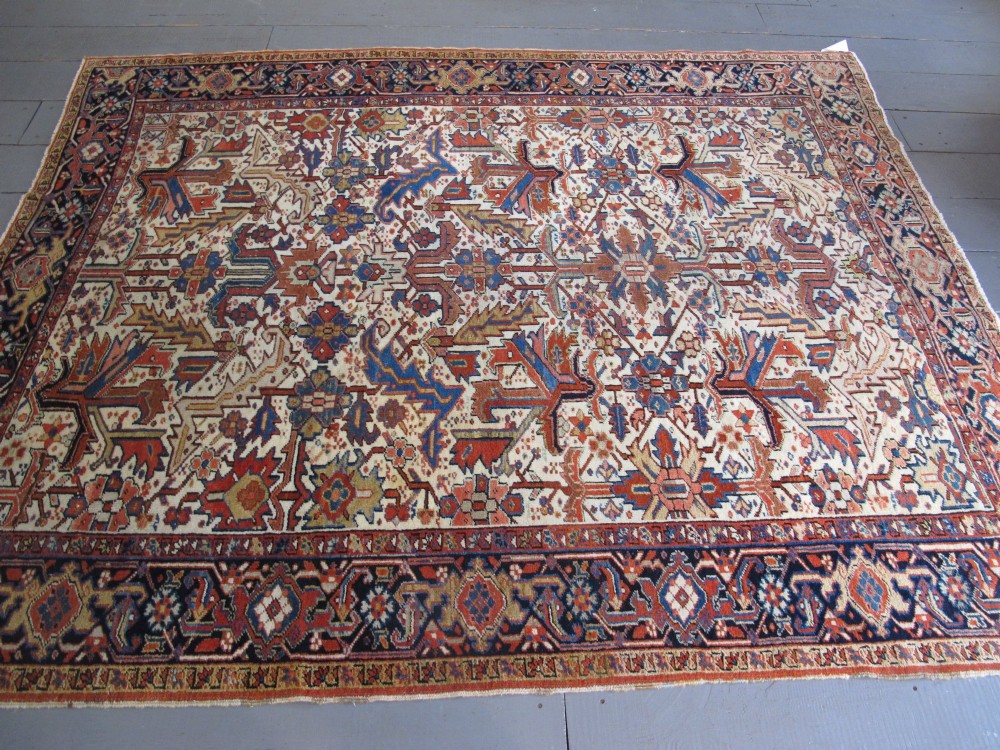 A large hand-knotted Persian Heriz rug featuring a central geometric medallion on an ivory background with terracotta and blue borders. View VIII