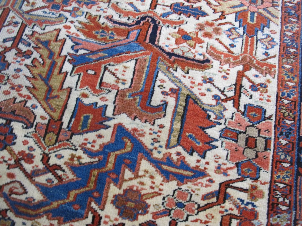 A large hand-knotted Persian Heriz rug featuring a central geometric medallion on an ivory background with terracotta and blue borders. View IX