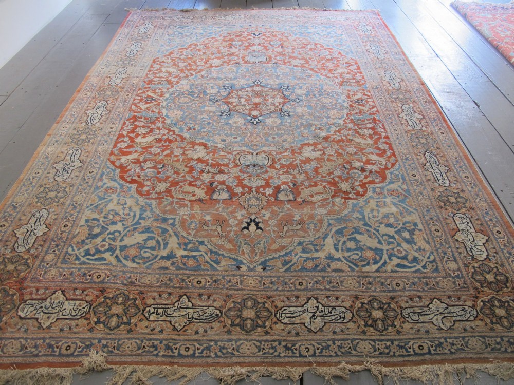 An antique Persian Tabriz carpet featuring a central medallion surrounded by floral motifs in terracotta and pale blue with calligraphic border cartouches.