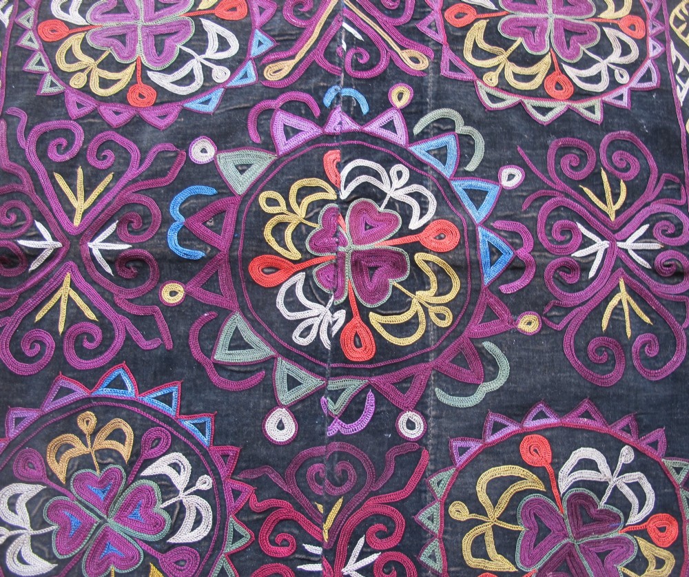 A square dark fabric mirror cover featuring intricate multicoloured silk chain stitch embroidery in circular solar motifs surrounded by a beaded fringe border. View II