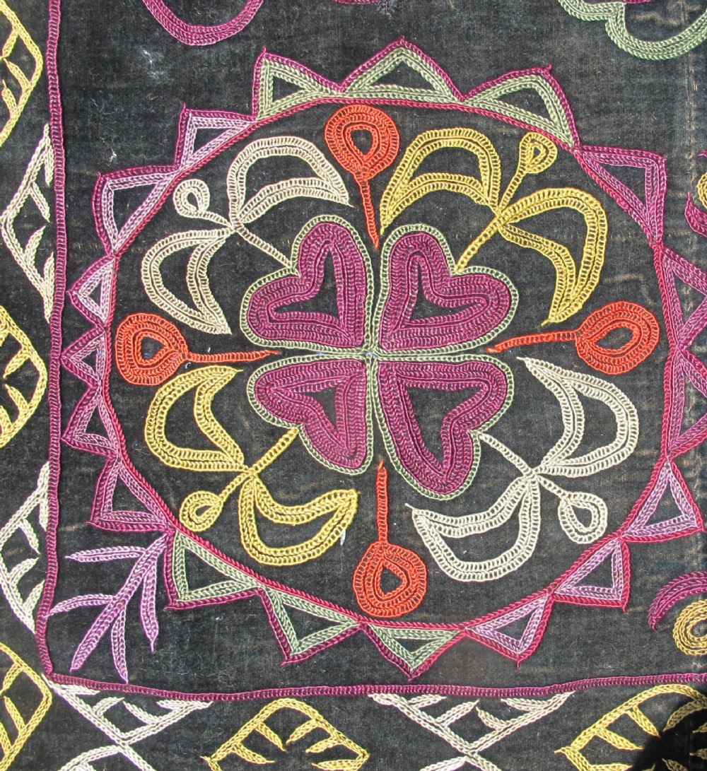 A square dark fabric mirror cover featuring intricate multicoloured silk chain stitch embroidery in circular solar motifs surrounded by a beaded fringe border. View IV
