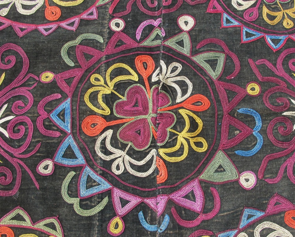 A square dark fabric mirror cover featuring intricate multicoloured silk chain stitch embroidery in circular solar motifs surrounded by a beaded fringe border. View V