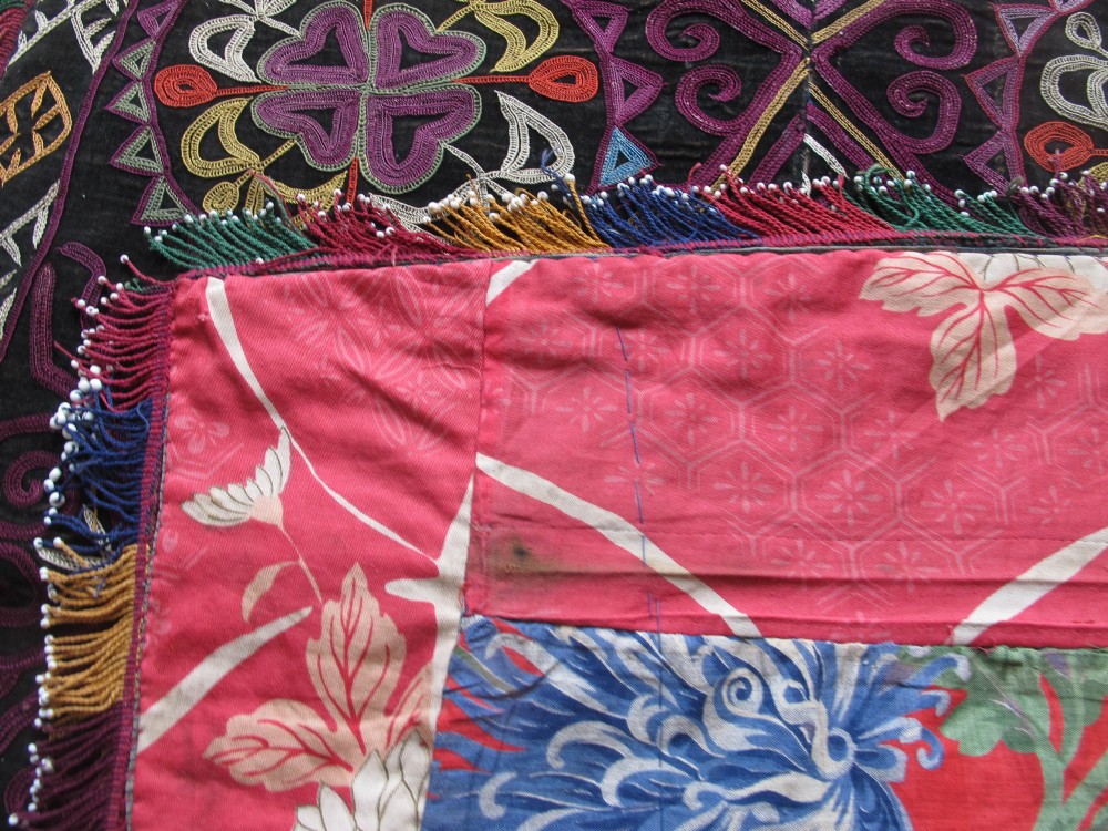A square dark fabric mirror cover featuring intricate multicoloured silk chain stitch embroidery in circular solar motifs surrounded by a beaded fringe border. View VI