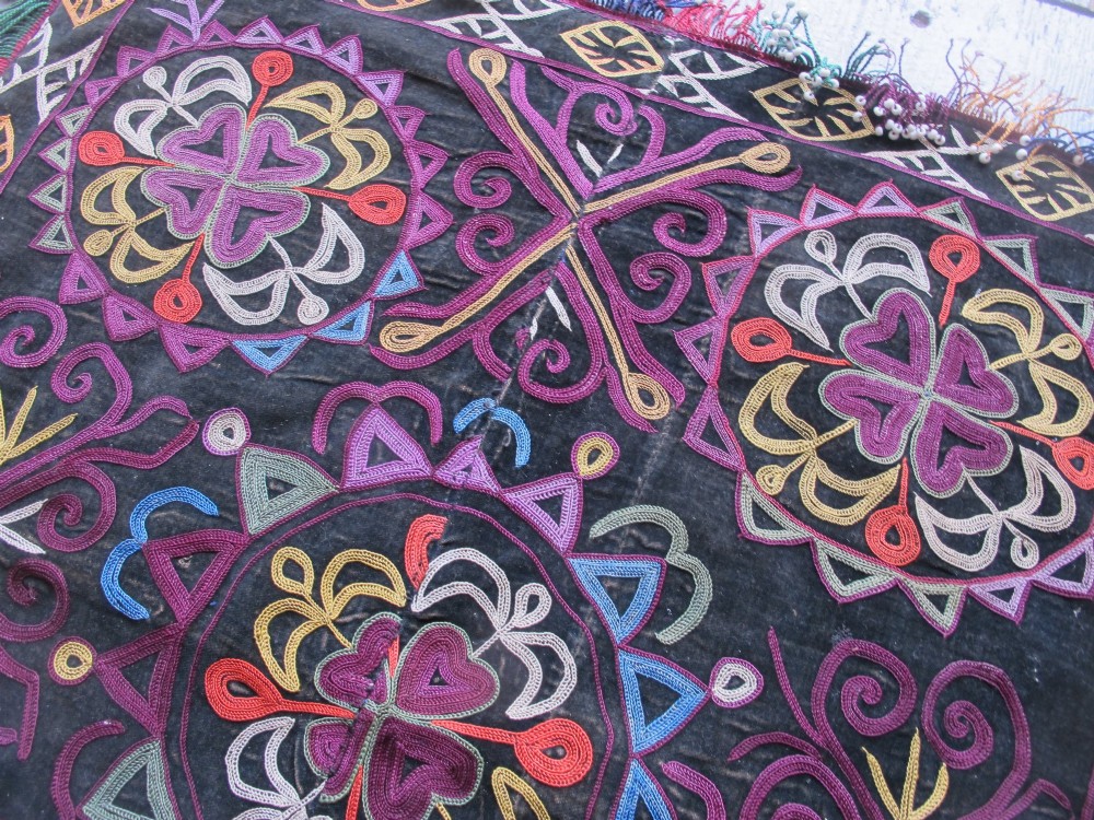 A square dark fabric mirror cover featuring intricate multicoloured silk chain stitch embroidery in circular solar motifs surrounded by a beaded fringe border. View VIII