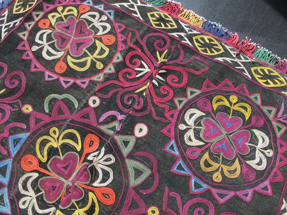 A square dark fabric mirror cover featuring intricate multicoloured silk chain stitch embroidery in circular solar motifs surrounded by a beaded fringe border. View XIII