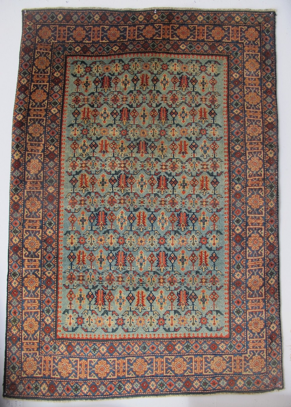 An antique Persian Tabriz wool rug featuring a light blue central field filled with repeating geometric floral motifs surrounded by multi-tiered terracotta and navy borders.