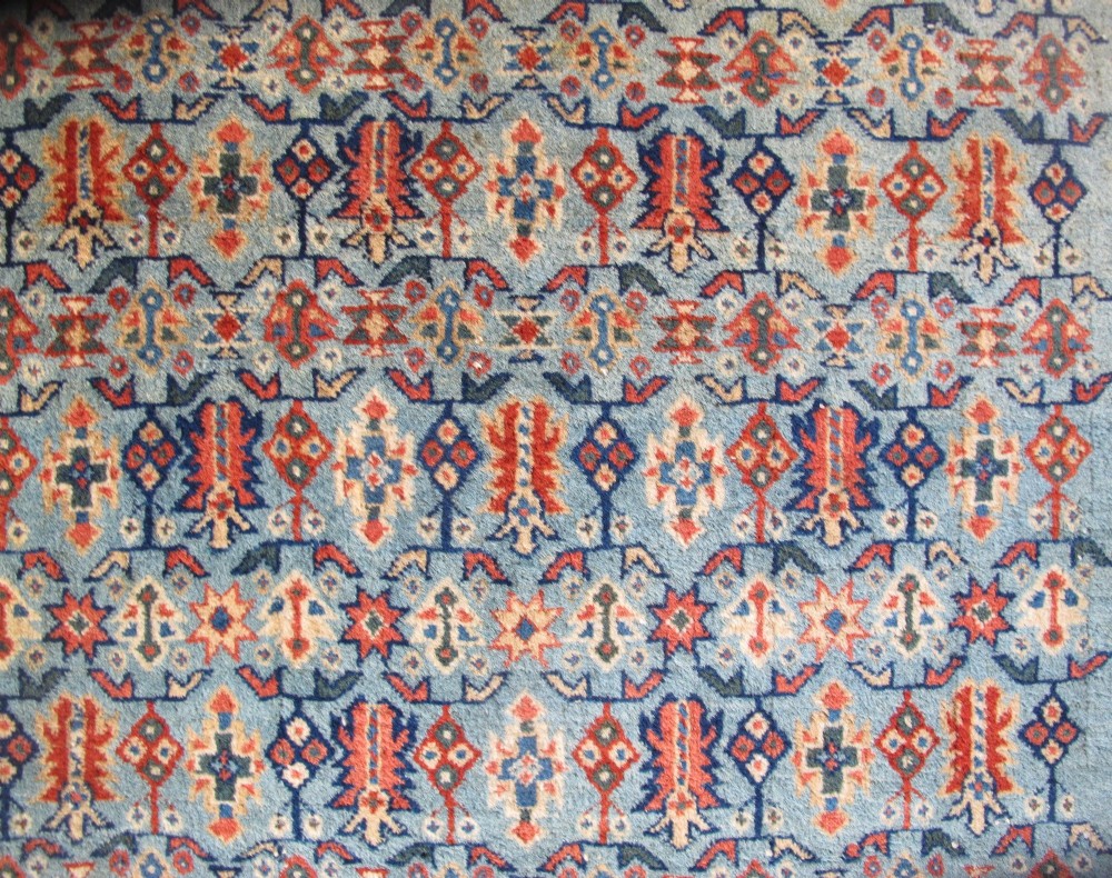 An antique Persian Tabriz wool rug featuring a light blue central field filled with repeating geometric floral motifs surrounded by multi-tiered terracotta and navy borders. View II