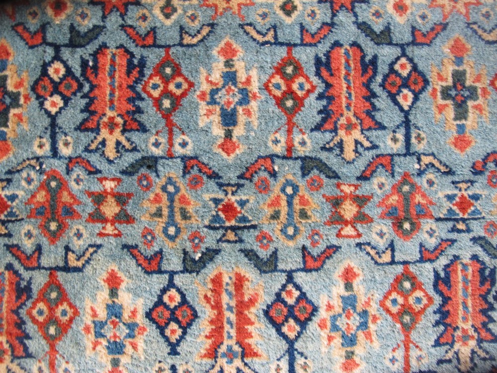 An antique Persian Tabriz wool rug featuring a light blue central field filled with repeating geometric floral motifs surrounded by multi-tiered terracotta and navy borders. View III