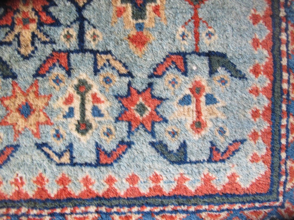 An antique Persian Tabriz wool rug featuring a light blue central field filled with repeating geometric floral motifs surrounded by multi-tiered terracotta and navy borders. View IV