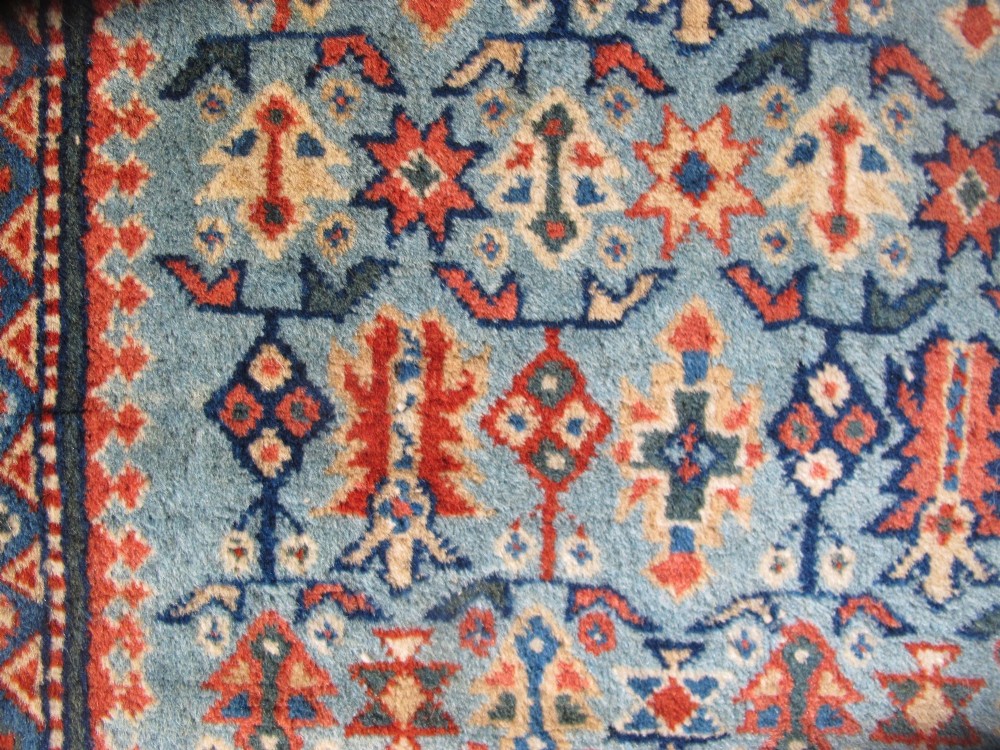An antique Persian Tabriz wool rug featuring a light blue central field filled with repeating geometric floral motifs surrounded by multi-tiered terracotta and navy borders. View V