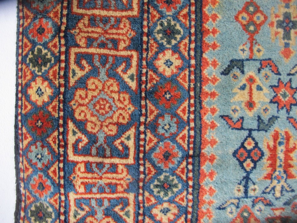 An antique Persian Tabriz wool rug featuring a light blue central field filled with repeating geometric floral motifs surrounded by multi-tiered terracotta and navy borders. View VII