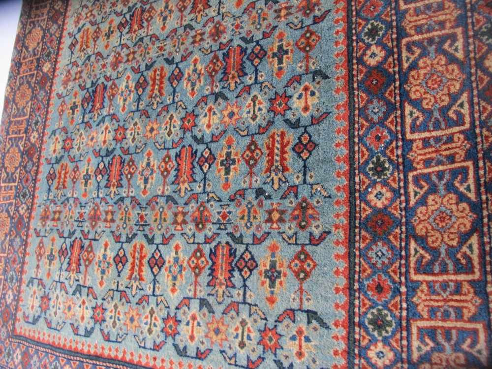 An antique Persian Tabriz wool rug featuring a light blue central field filled with repeating geometric floral motifs surrounded by multi-tiered terracotta and navy borders. View IX