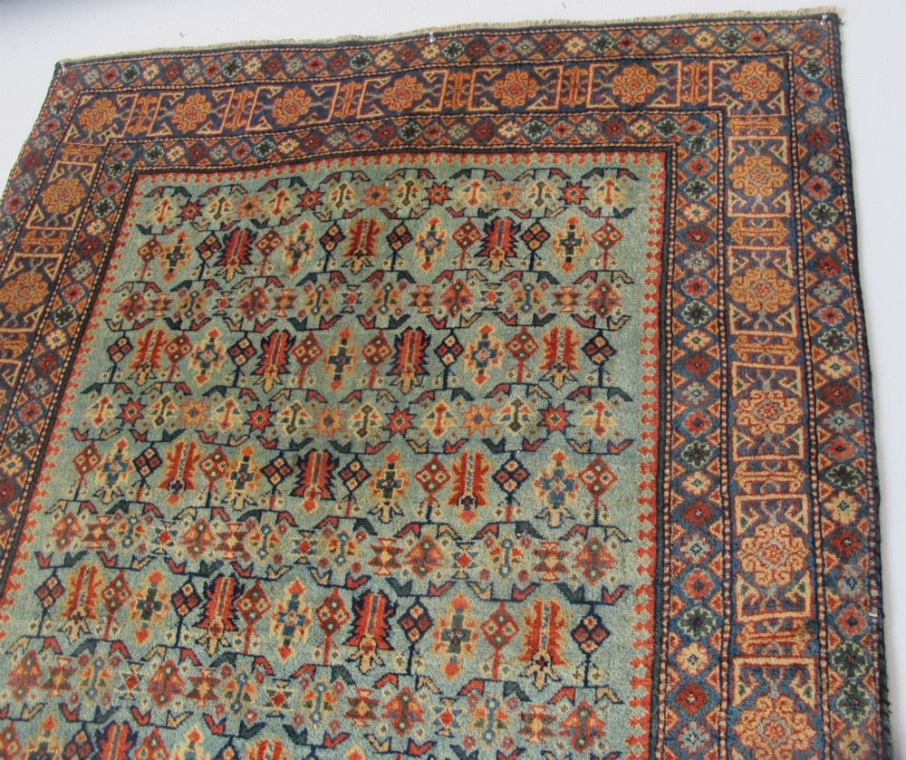 An antique Persian Tabriz wool rug featuring a light blue central field filled with repeating geometric floral motifs surrounded by multi-tiered terracotta and navy borders. View X