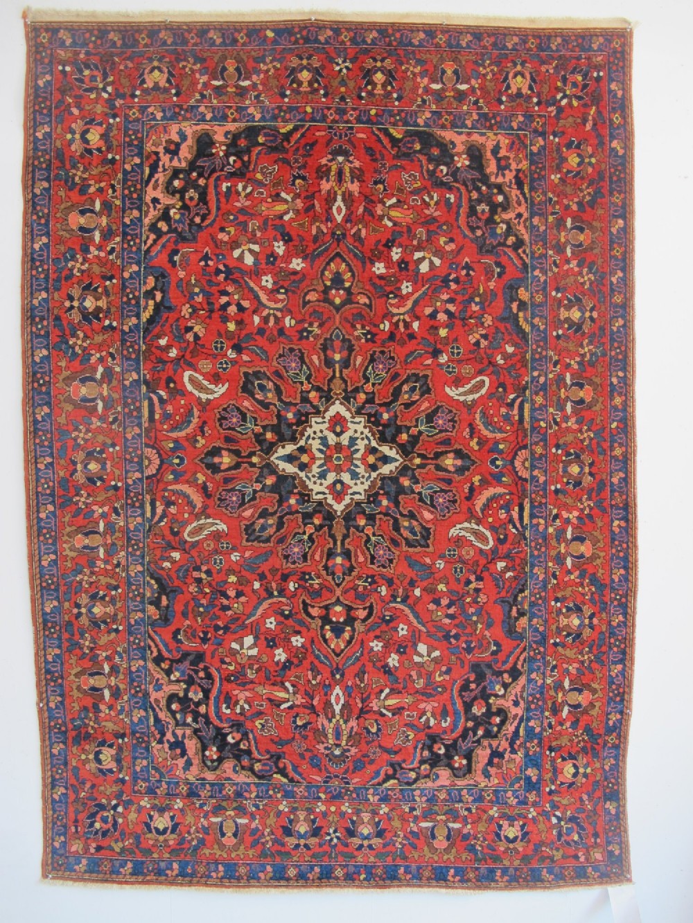 An antique Persian Bakhtiar hand-knotted wool rug featuring a central ivory and blue lobed medallion on a rich red field with floral motifs, surrounded by dark blue spandrels and borders.