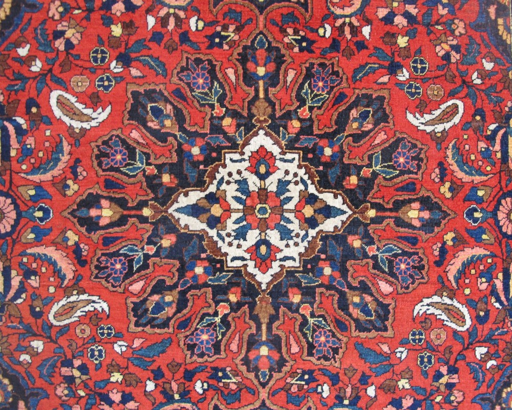 An antique Persian Bakhtiar hand-knotted wool rug featuring a central ivory and blue lobed medallion on a rich red field with floral motifs, surrounded by dark blue spandrels and borders. View II