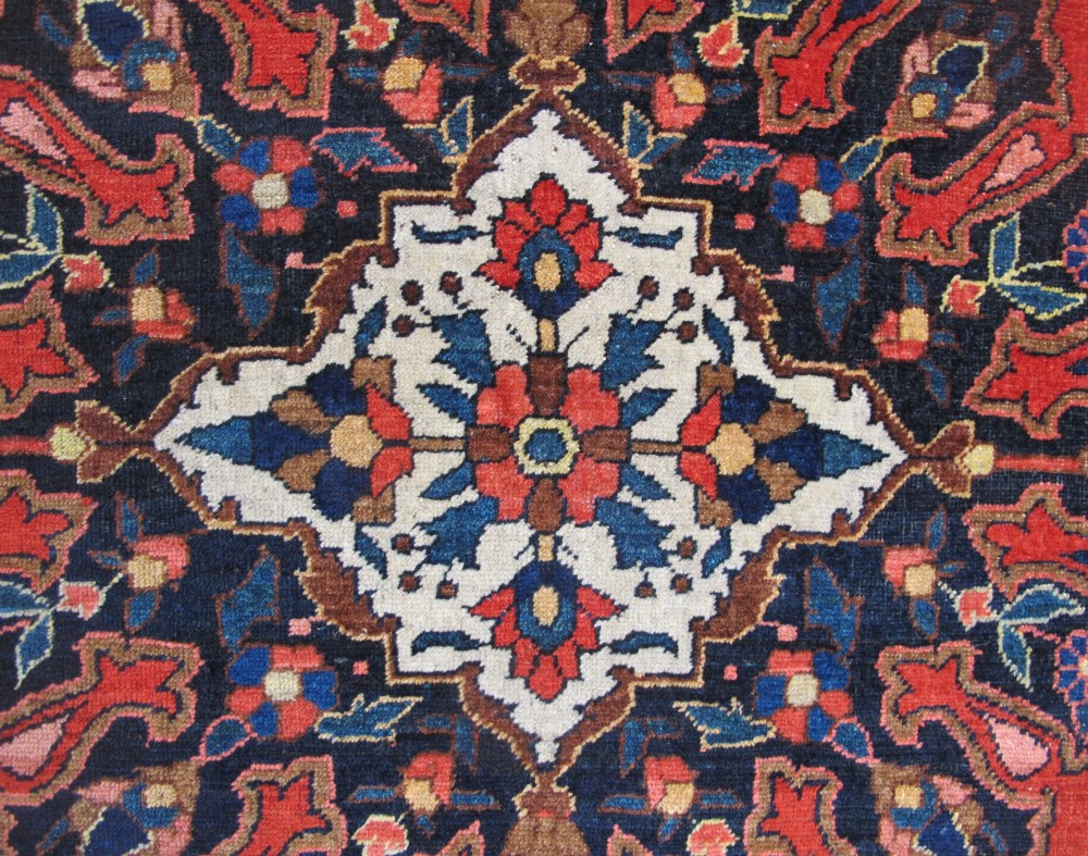 An antique Persian Bakhtiar hand-knotted wool rug featuring a central ivory and blue lobed medallion on a rich red field with floral motifs, surrounded by dark blue spandrels and borders. View III