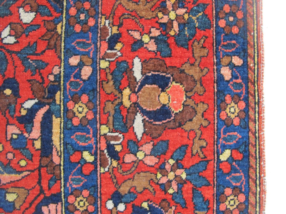 An antique Persian Bakhtiar hand-knotted wool rug featuring a central ivory and blue lobed medallion on a rich red field with floral motifs, surrounded by dark blue spandrels and borders. View IV