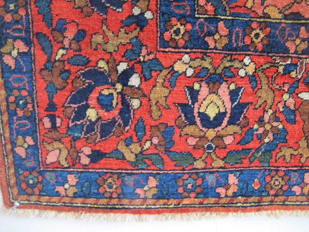 An antique Persian Bakhtiar hand-knotted wool rug featuring a central ivory and blue lobed medallion on a rich red field with floral motifs, surrounded by dark blue spandrels and borders. View VII