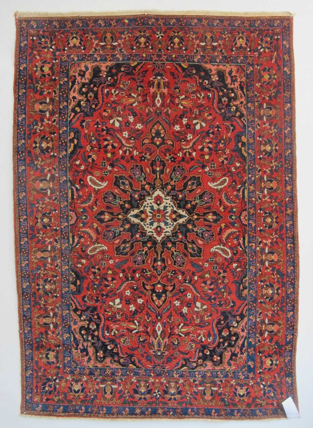An antique Persian Bakhtiar hand-knotted wool rug featuring a central ivory and blue lobed medallion on a rich red field with floral motifs, surrounded by dark blue spandrels and borders. View IX