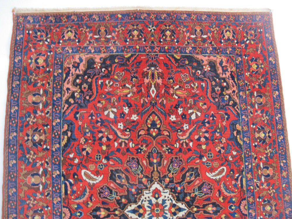 An antique Persian Bakhtiar hand-knotted wool rug featuring a central ivory and blue lobed medallion on a rich red field with floral motifs, surrounded by dark blue spandrels and borders. View X