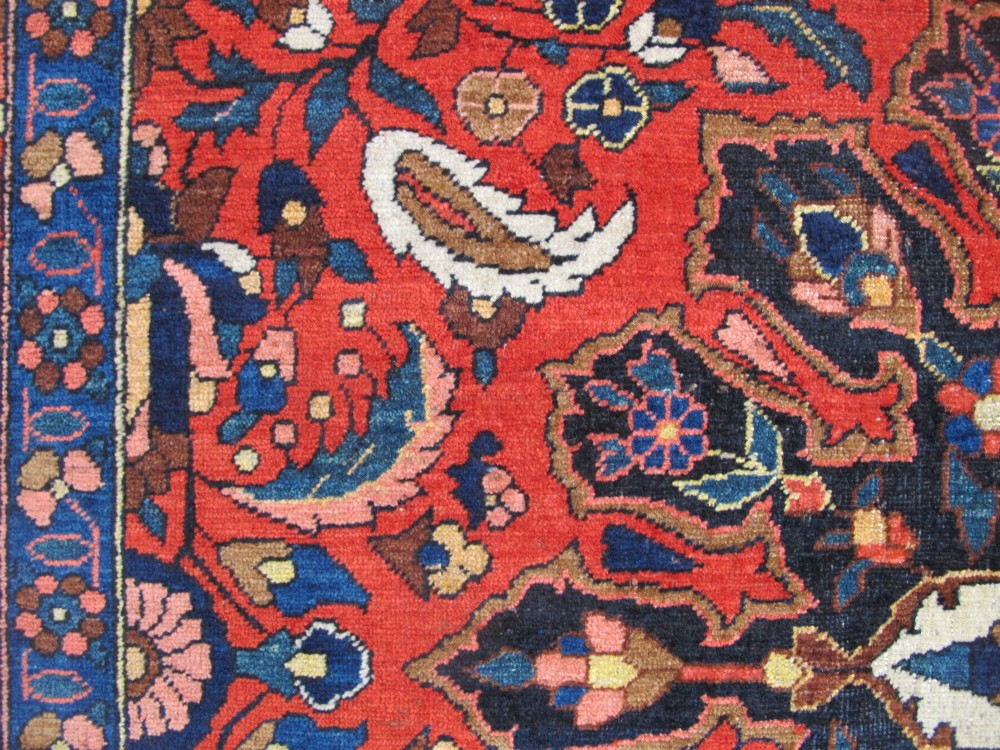 An antique Persian Bakhtiar hand-knotted wool rug featuring a central ivory and blue lobed medallion on a rich red field with floral motifs, surrounded by dark blue spandrels and borders. View XII