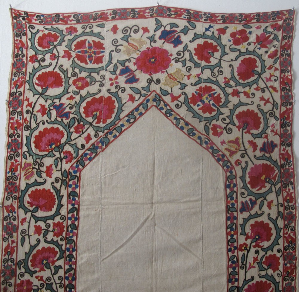 An antique cream cotton suzani textile embroidered with an architectural arch and red floral vines with teal leaves. View II