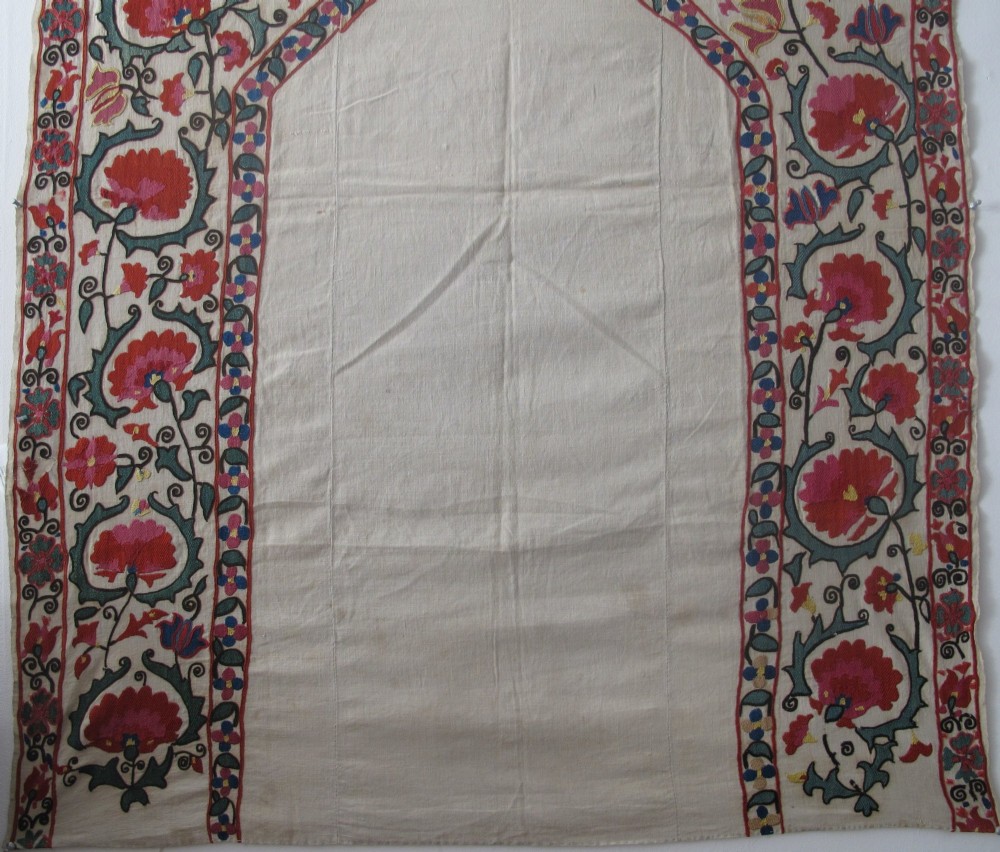 An antique cream cotton suzani textile embroidered with an architectural arch and red floral vines with teal leaves. View III