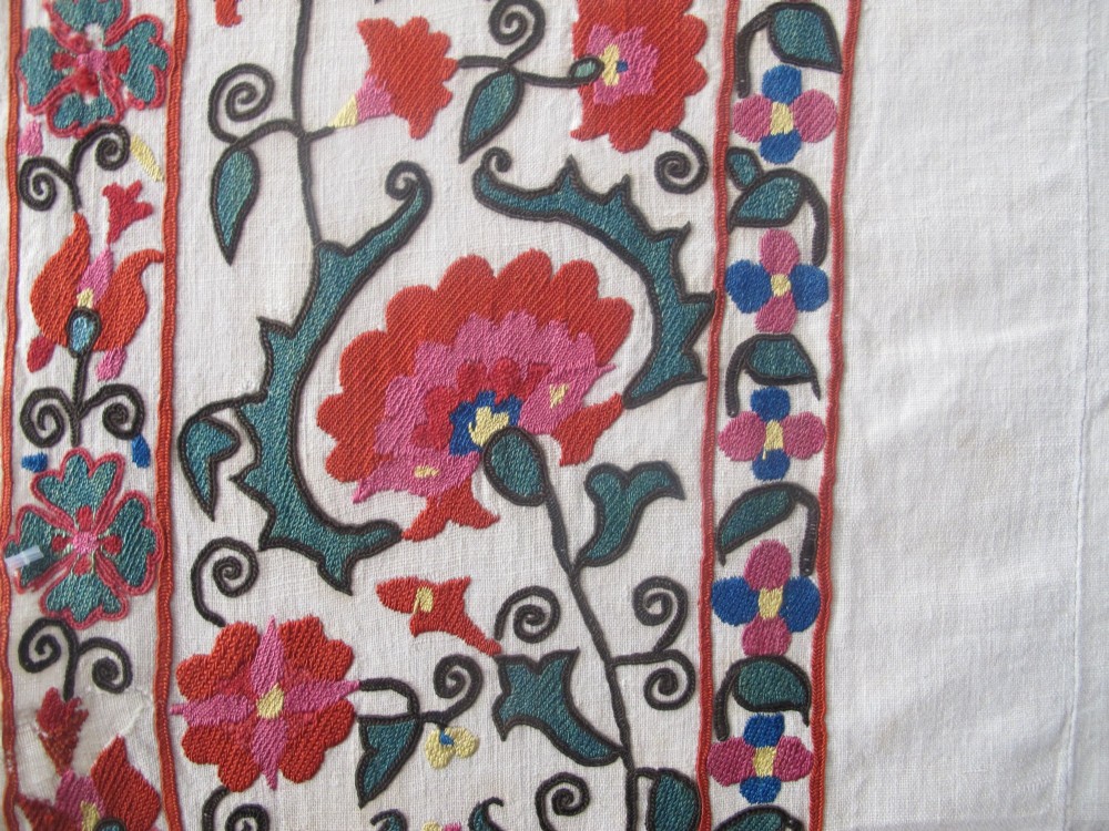 An antique cream cotton suzani textile embroidered with an architectural arch and red floral vines with teal leaves. View IV