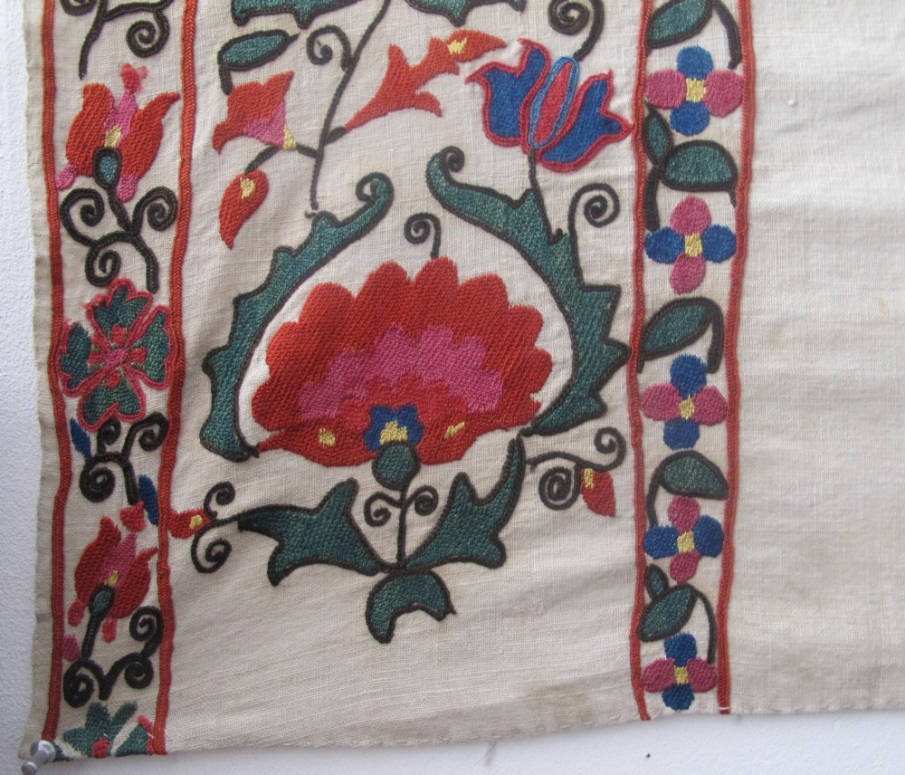 An antique cream cotton suzani textile embroidered with an architectural arch and red floral vines with teal leaves. View V