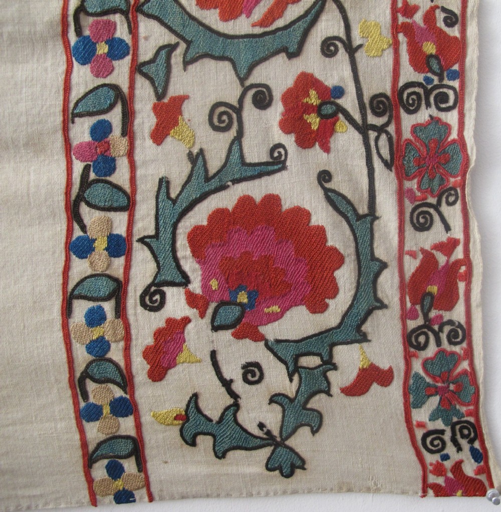 An antique cream cotton suzani textile embroidered with an architectural arch and red floral vines with teal leaves. View VI