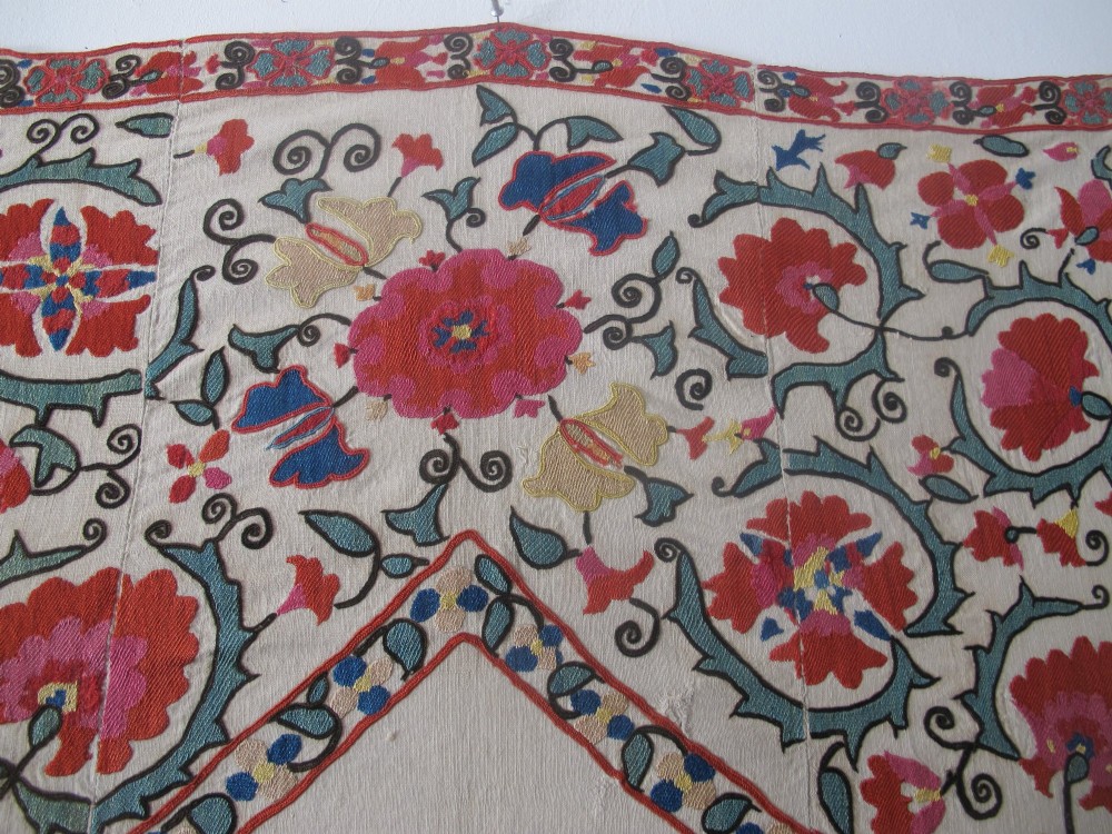 An antique cream cotton suzani textile embroidered with an architectural arch and red floral vines with teal leaves. View IX