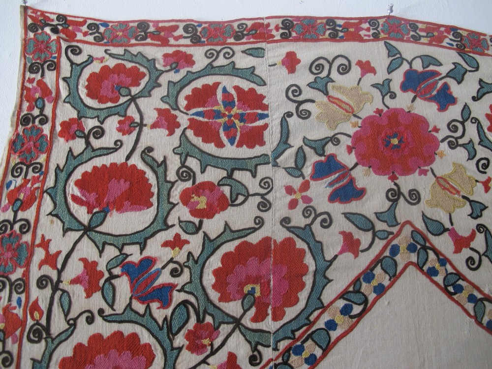 An antique cream cotton suzani textile embroidered with an architectural arch and red floral vines with teal leaves. View X