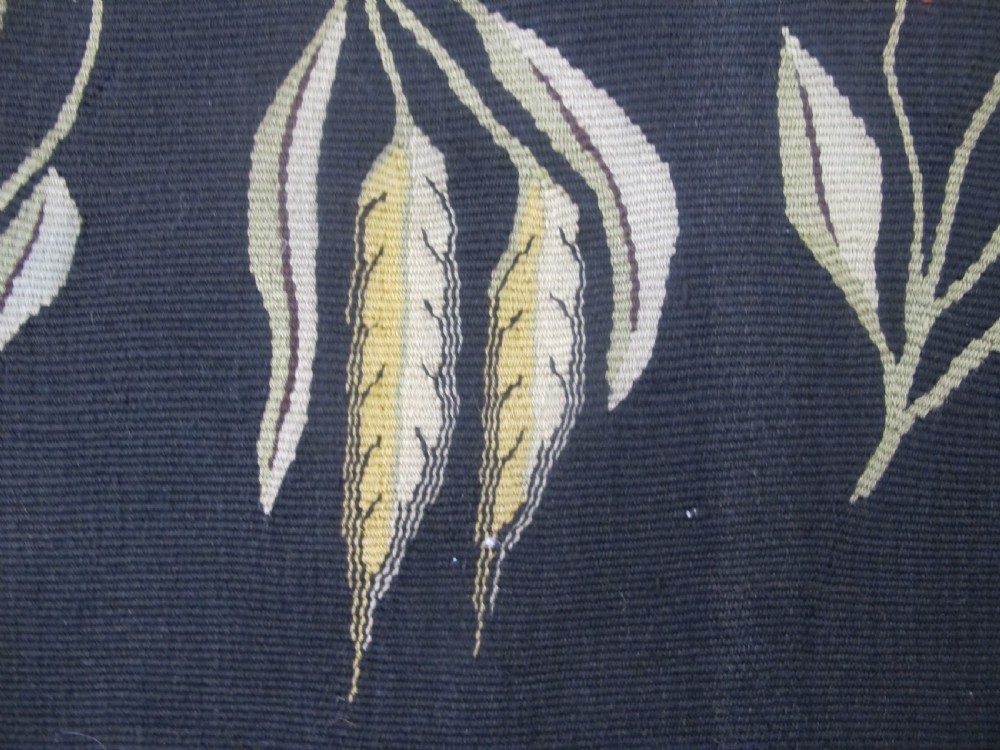 A rectangular black flatwoven wool tapestry featuring repeating stylised colourful botanical flowers and a geometric zigzag border. View VII