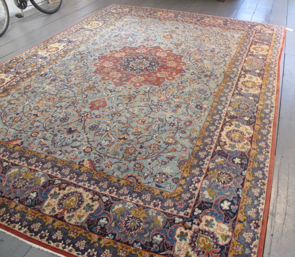 An early twentieth-century hand-knotted Persian Kashan wool carpet featuring a reddish central medallion on a light blue field surrounded by a navy floral border.