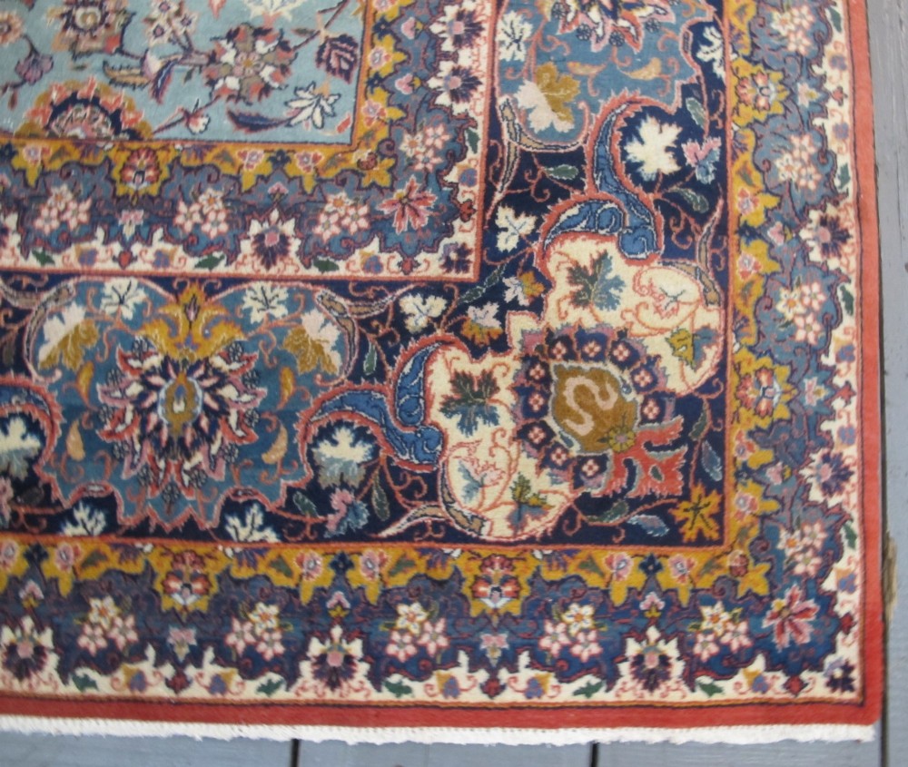 An early twentieth-century hand-knotted Persian Kashan wool carpet featuring a reddish central medallion on a light blue field surrounded by a navy floral border. View V