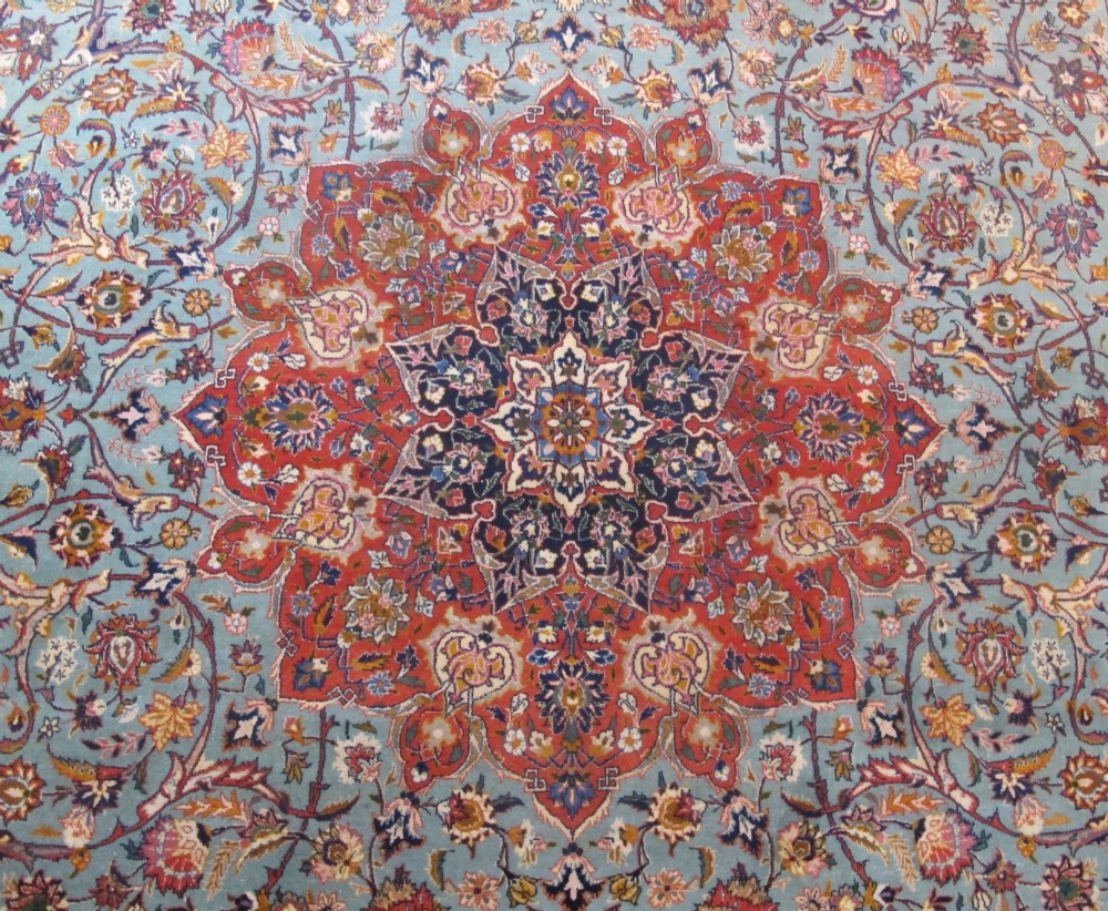 An early twentieth-century hand-knotted Persian Kashan wool carpet featuring a reddish central medallion on a light blue field surrounded by a navy floral border. View VI