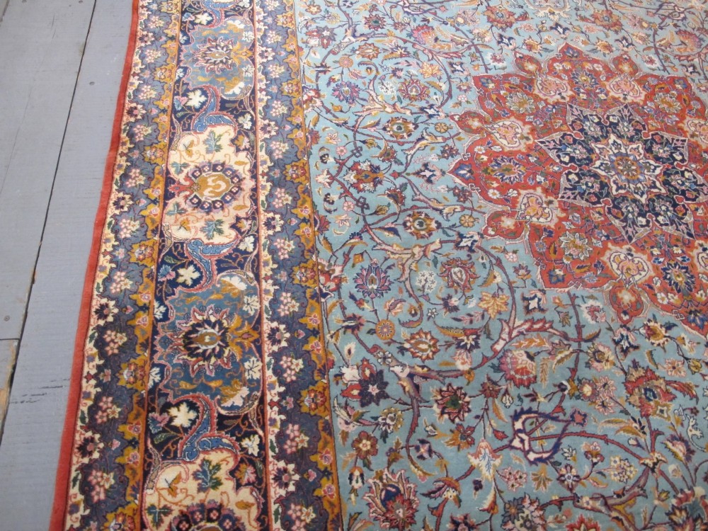 An early twentieth-century hand-knotted Persian Kashan wool carpet featuring a reddish central medallion on a light blue field surrounded by a navy floral border. View IX