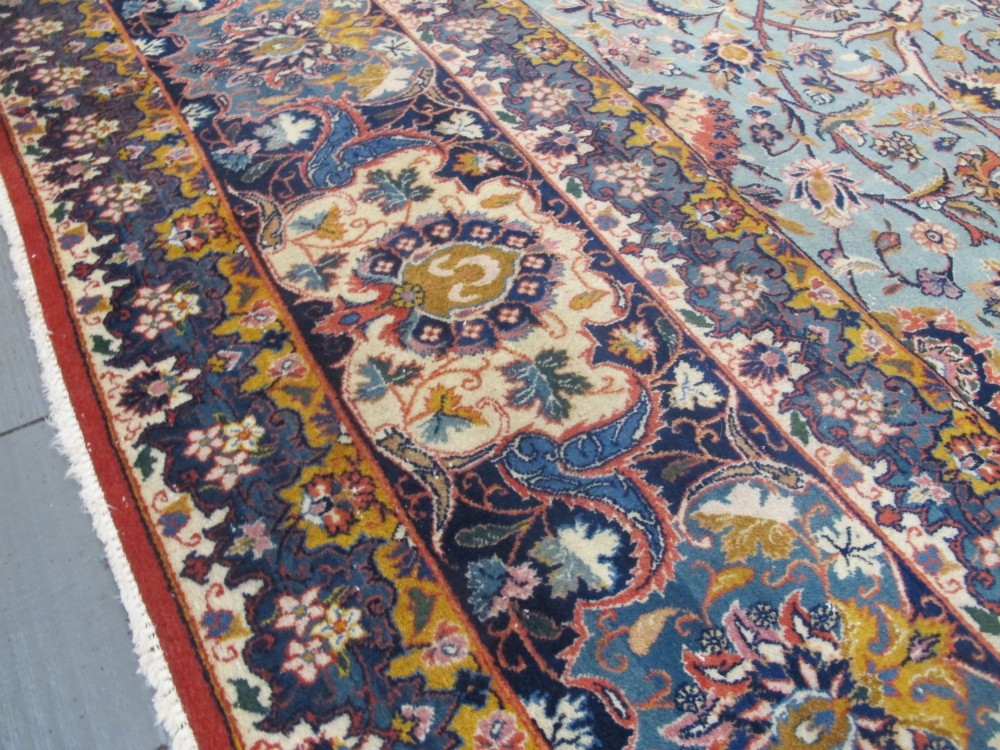 An early twentieth-century hand-knotted Persian Kashan wool carpet featuring a reddish central medallion on a light blue field surrounded by a navy floral border. View X
