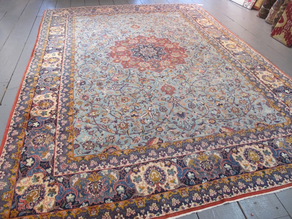 An early twentieth-century hand-knotted Persian Kashan wool carpet featuring a reddish central medallion on a light blue field surrounded by a navy floral border. View XII