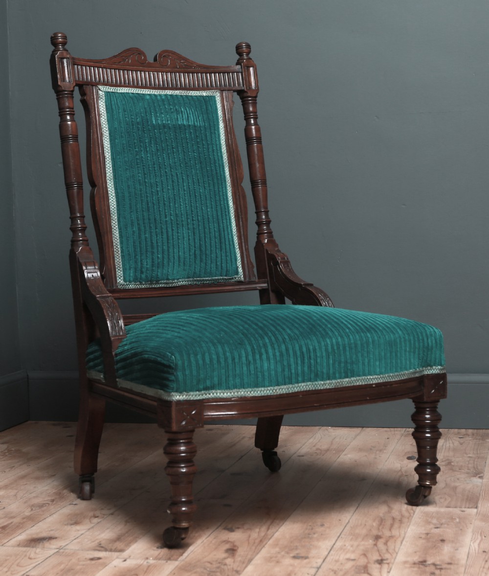 A Victorian carved walnut fireside chair featuring green corded upholstery, turned legs on castors, and decorative backrest details.
