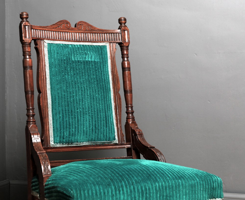 A Victorian carved walnut fireside chair featuring green corded upholstery, turned legs on castors, and decorative backrest details. View II