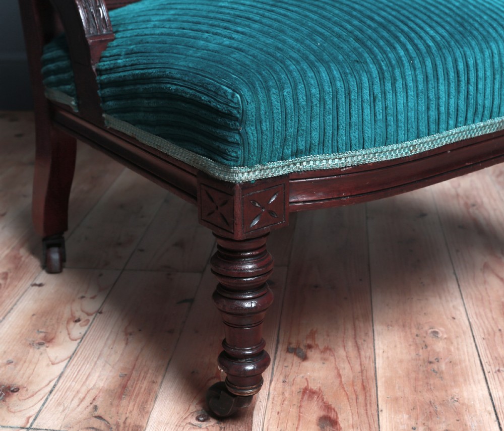 A Victorian carved walnut fireside chair featuring green corded upholstery, turned legs on castors, and decorative backrest details. View V