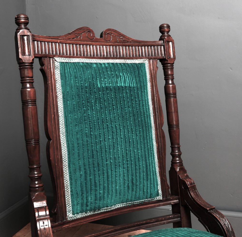 A Victorian carved walnut fireside chair featuring green corded upholstery, turned legs on castors, and decorative backrest details. View VII