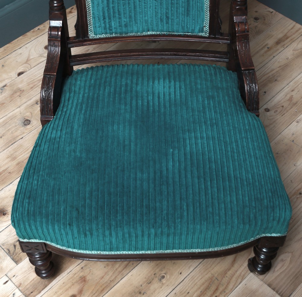 A Victorian carved walnut fireside chair featuring green corded upholstery, turned legs on castors, and decorative backrest details. View VIII