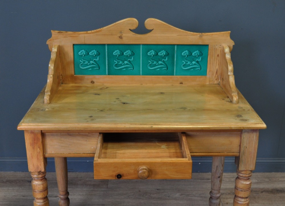 An antique Victorian pine washstand featuring a raised gallery splashback set with four green embossed tiles, a single frieze drawer, and turned legs. View III